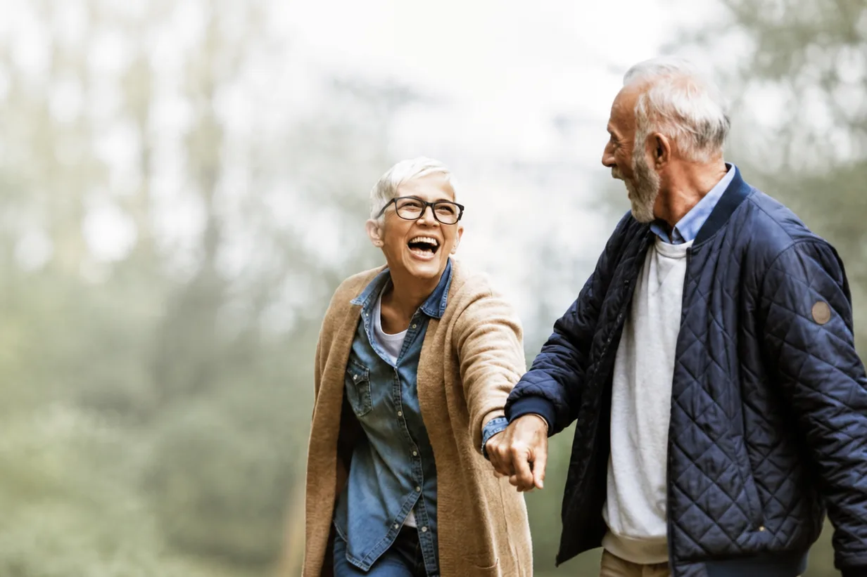 An older couple laughing together as they walk hand in hand through parkland